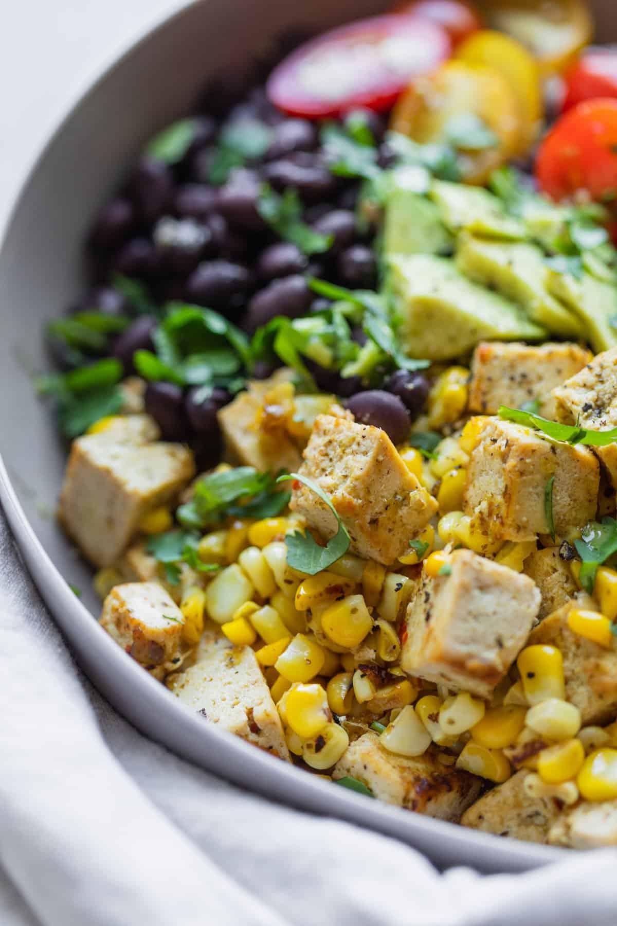 A close-up of a person assembling a Black Bean and Corn Tofu Rice Bowl