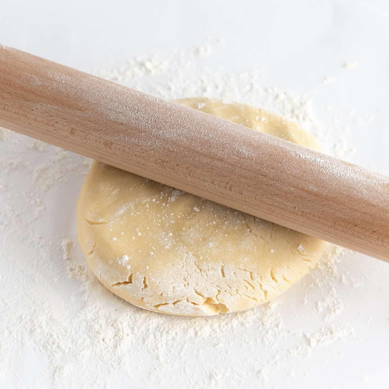 a baker's hands gently pressing cookie dough with a rolling pin on a floured surface