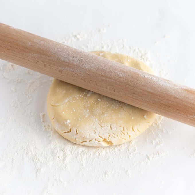 Hands rolling out cocoa cookie dough with a rolling pin and cookie cutters nearby