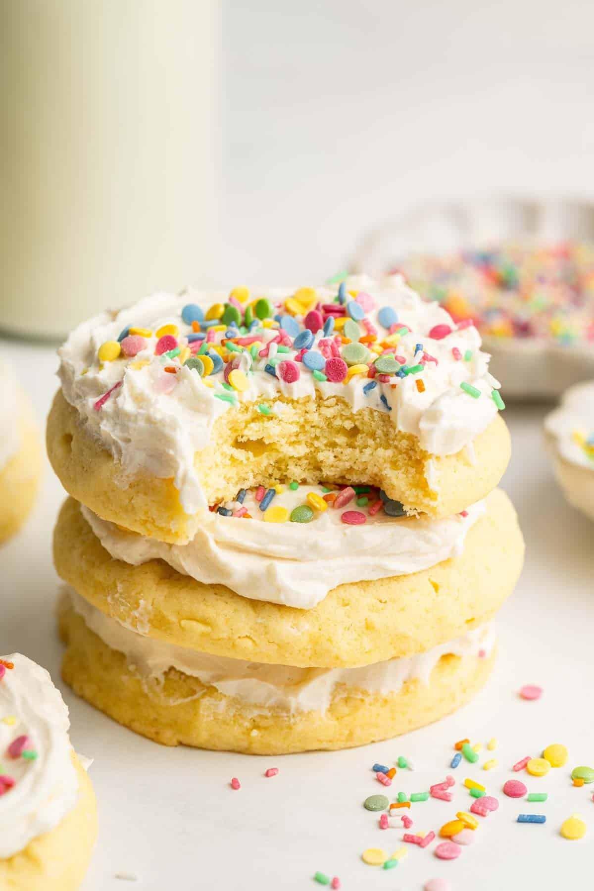 stack of freshly baked sugar cookies with sprinkles and a bowl of vanilla icing