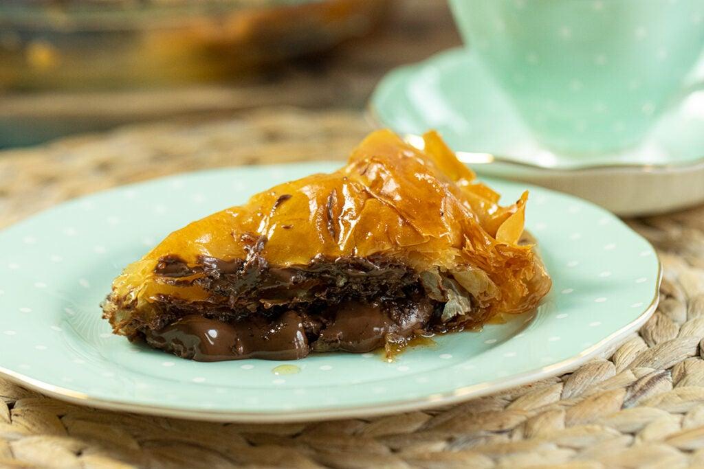 Close-up shot of a slice of hazelnut baklava drizzled with chocolate ganache, showcasing flaky layers