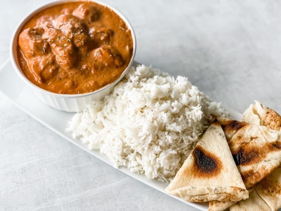 moonlight butter chicken being served over basmati rice with a side of naan bread