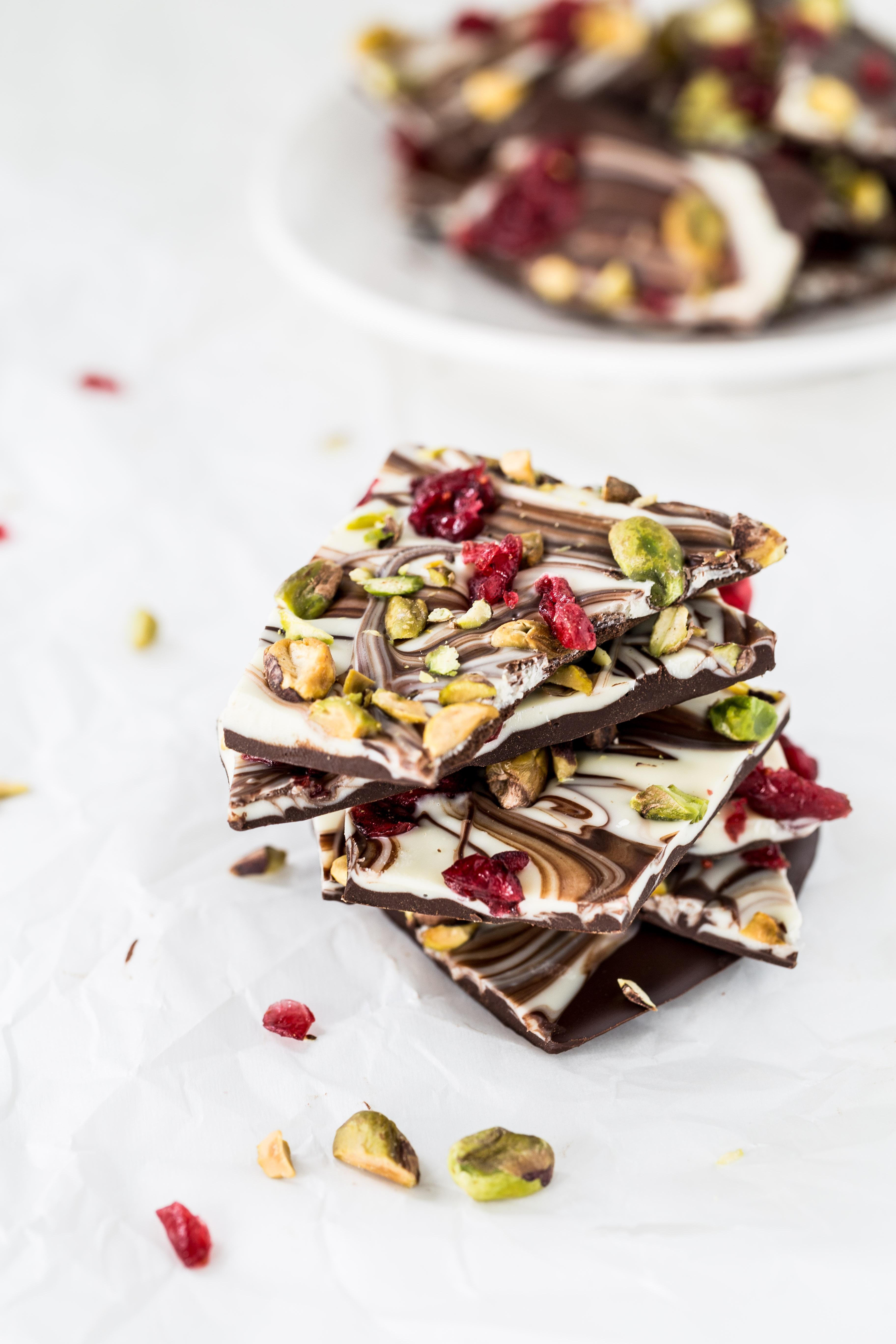 Hands sprinkling various toppings like pistachios and cranberries onto cooling swirled chocolate bark