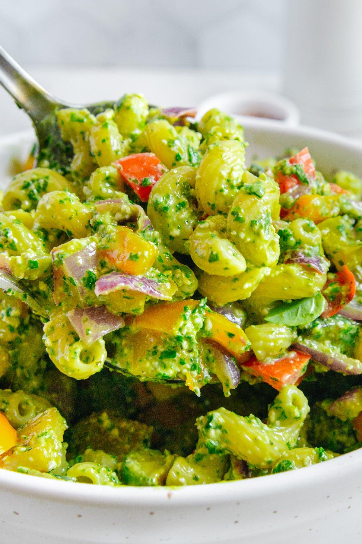 a close-up shot of roasted vegetables being tossed with quinoa pasta and pesto