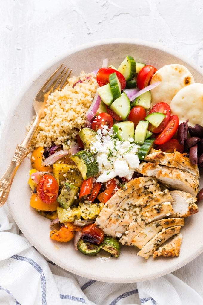 Assembled chicken souvlaki bowl with quinoa, grilled chicken, avocado crema, tomatoes, and cucumbers
