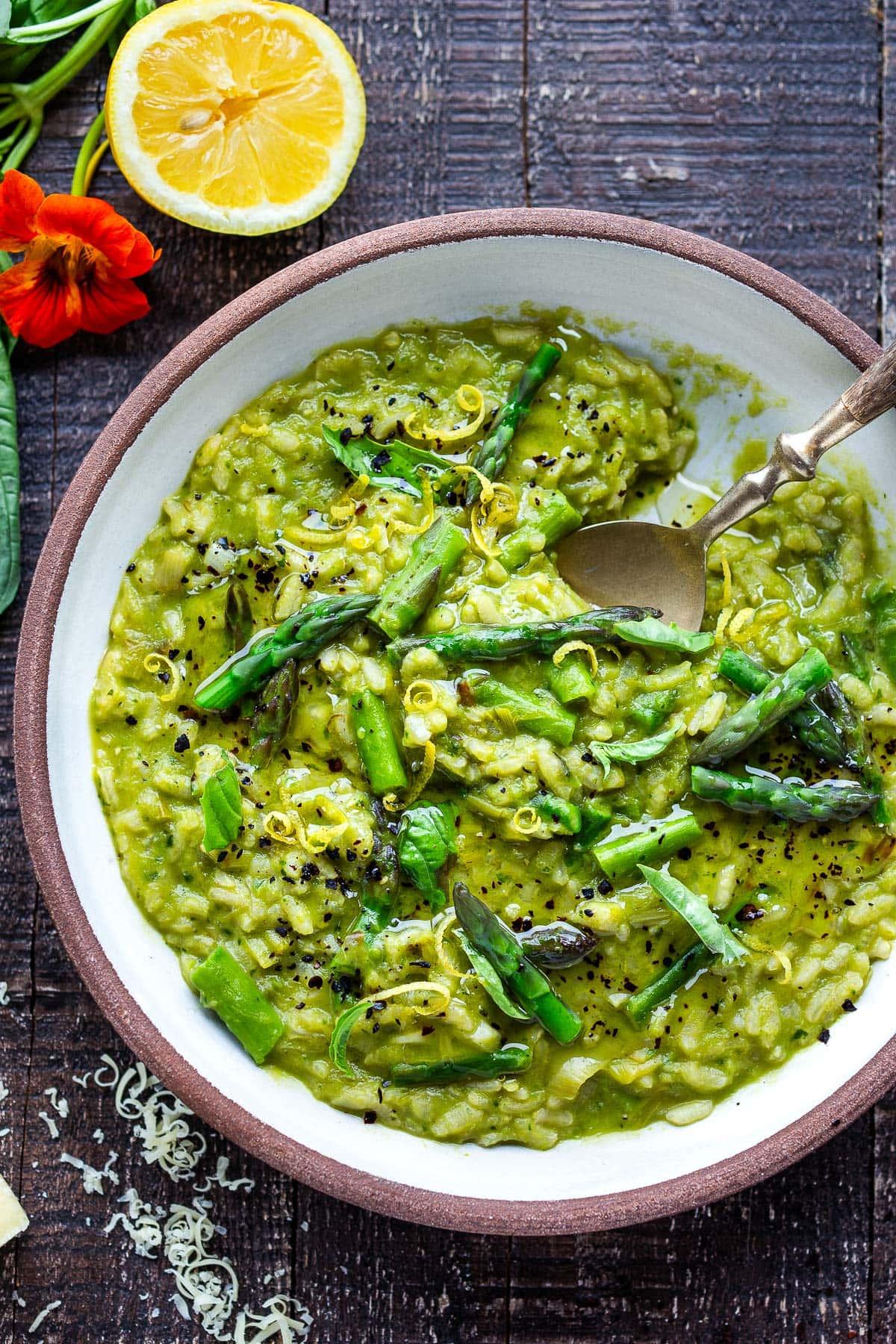 a bowl of spicy asparagus risotto next to fresh asparagus spears and chili flakes
