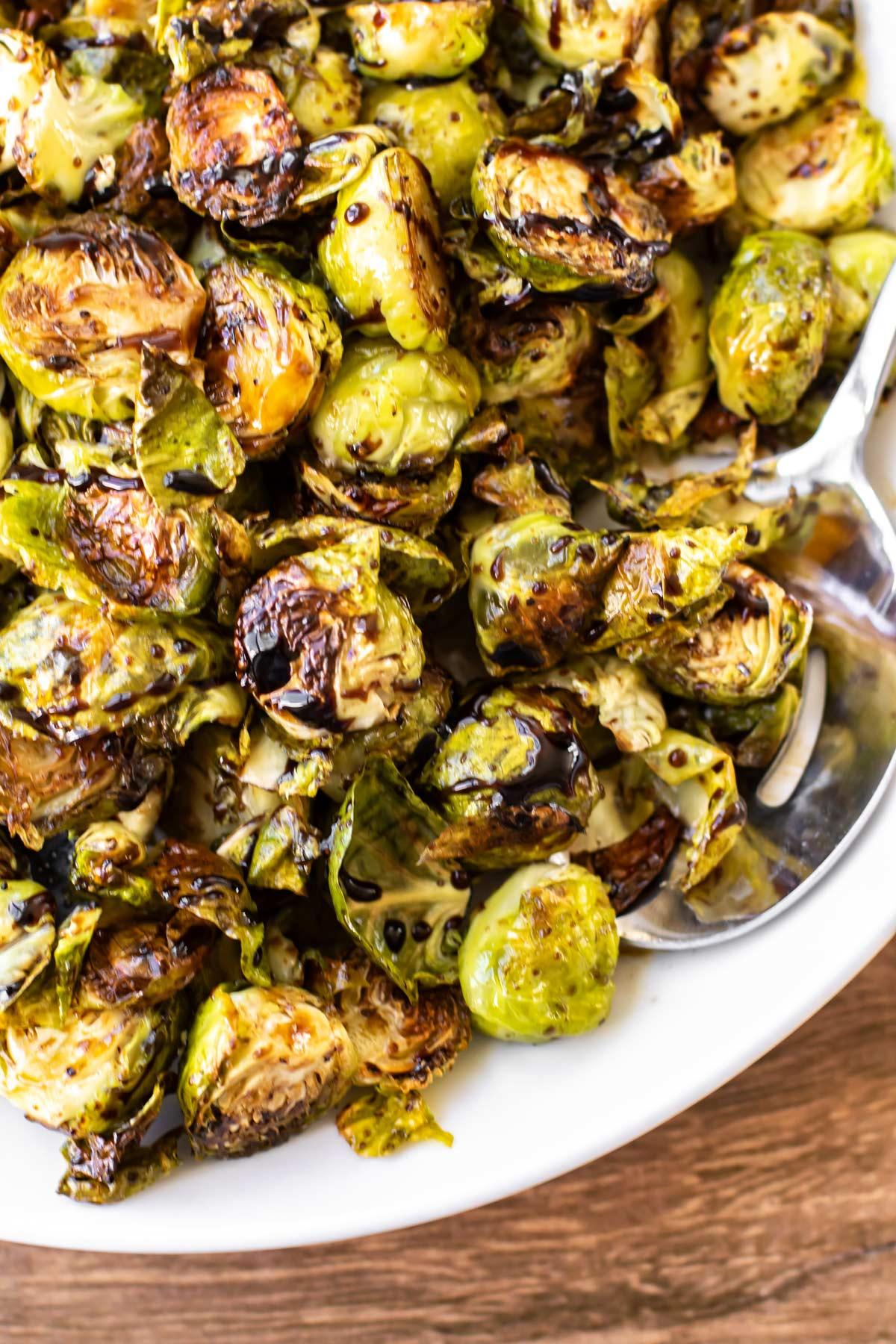 Platter of roasted Brussels sprouts with balsamic glaze garnished with fresh herbs, ready to serve