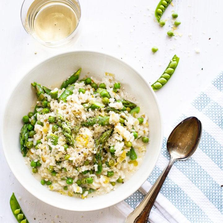 Overhead shot of a finished Spring Asparagus Risotto with Preserved Lemon in a bowl, garnished with fresh herbs and Parmesan cheese