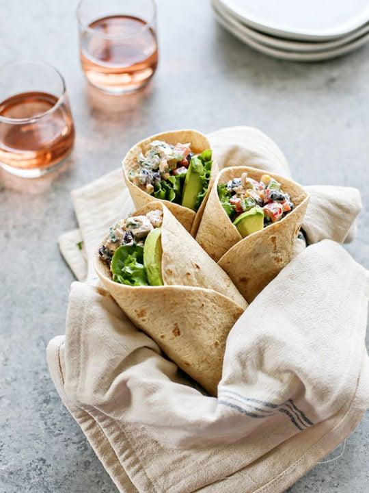 A beautifully assembled hearty chicken wrap, cut in half, with fresh ingredients visible, on a wooden cutting board with a side salad and dipping sauce.