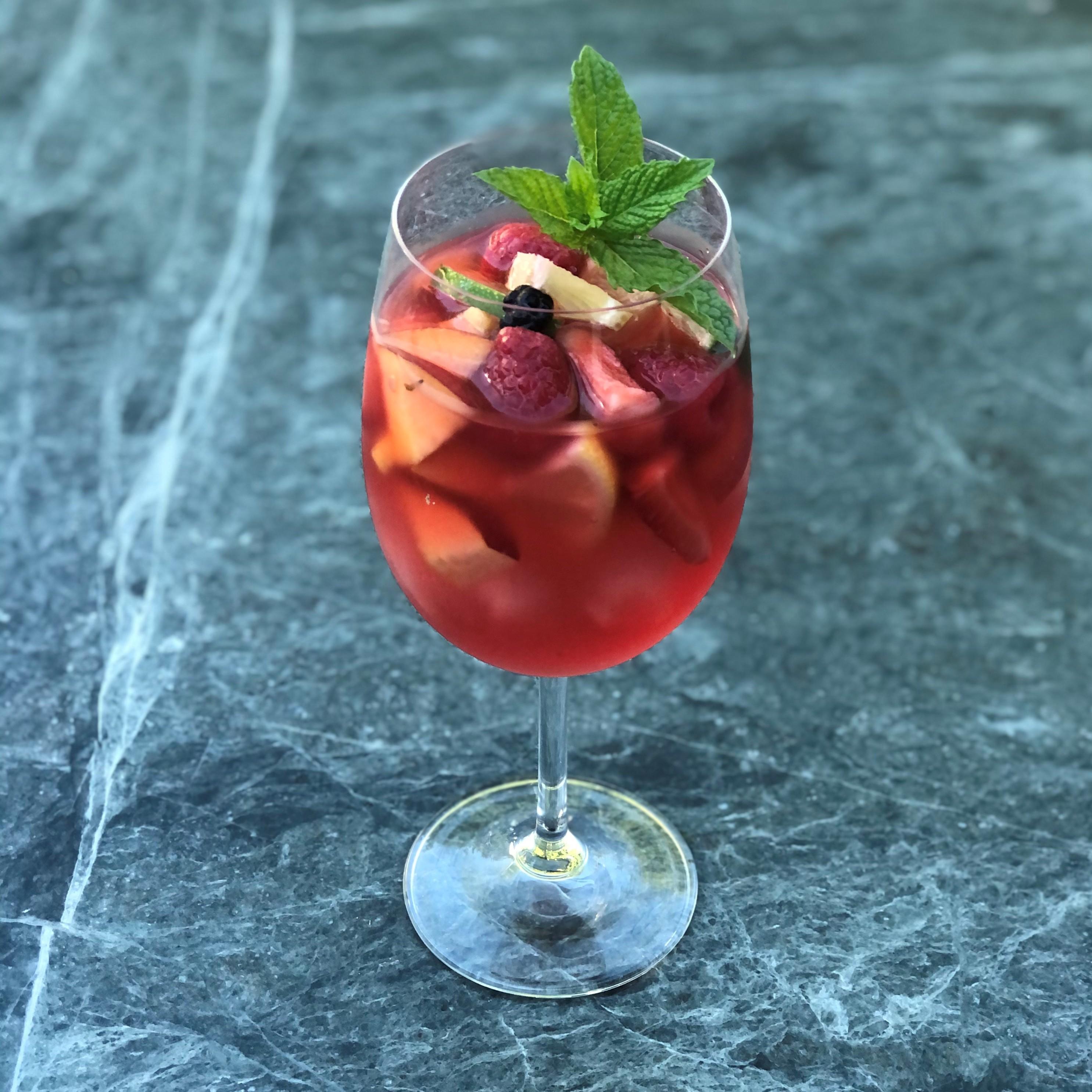 A pitcher of raspberry rosé sangria garnished with fruit and mint