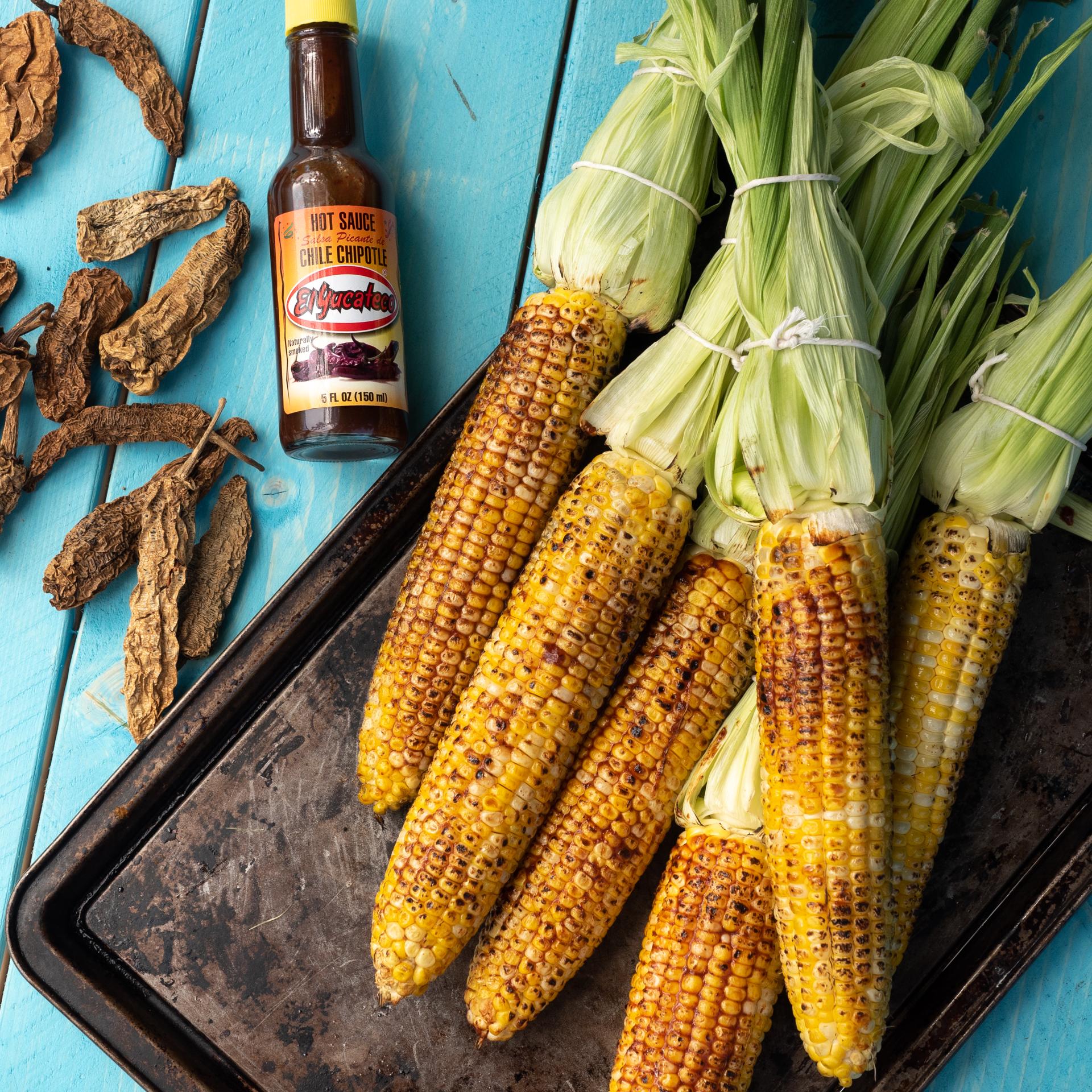 Someone brushing chipotle aioli onto grilled corn on the cob