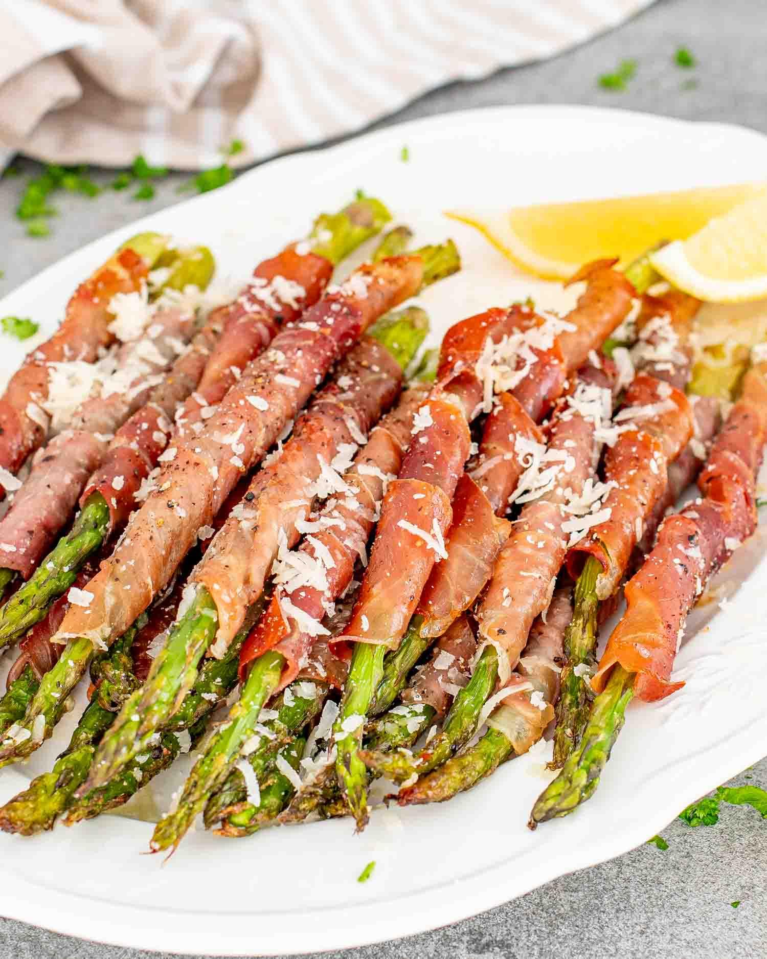 Close-up of crispy prosciutto wrapped asparagus spears on a serving platter with lemon wedges