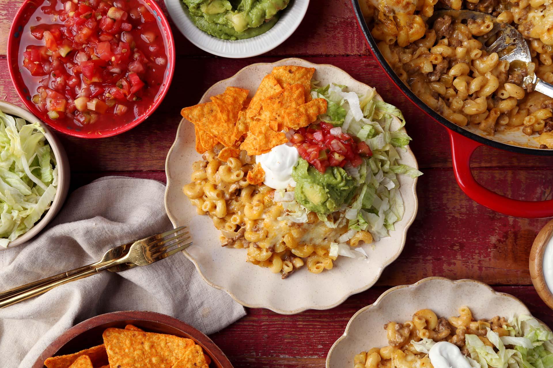 A wide shot of a table set for a casual dinner party, featuring Taco Mac and Cheese as the main dish.