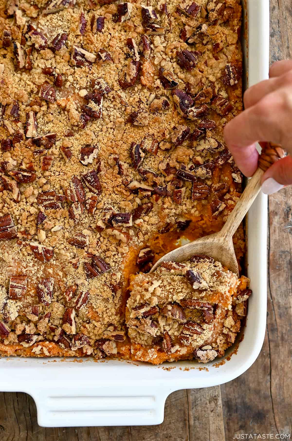 Hands scooping creamy sweet potato casserole from a dish