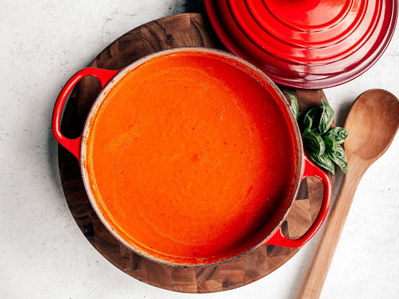 Close-up of vibrant red tomato soup simmering in a Dutch oven, steam rising