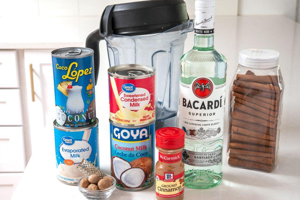 Ingredients for Coquito laid out on a kitchen counter: cans of milk, rum bottle, spices