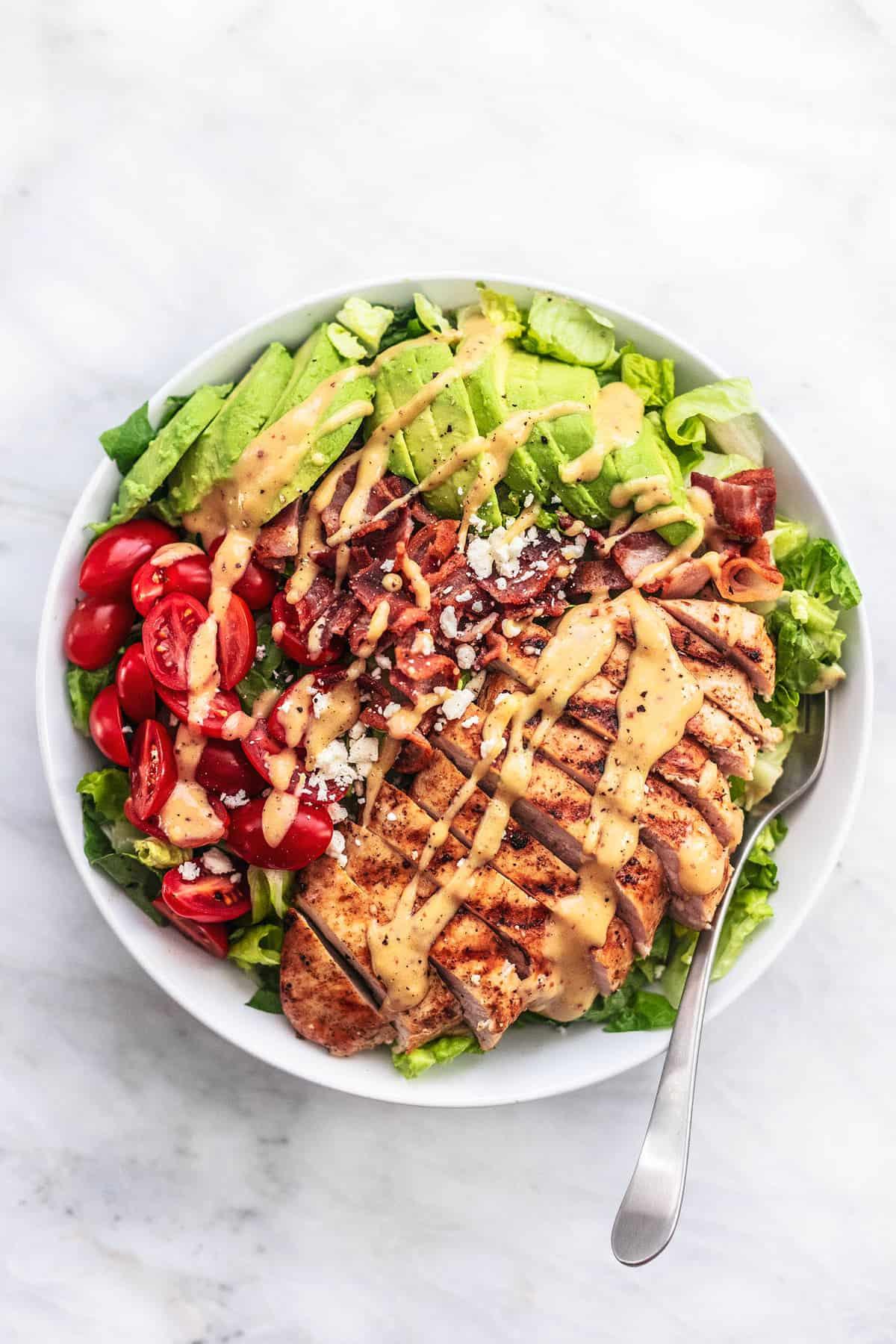 a plate of salad with grilled chicken, avocado, and parmesan cheese