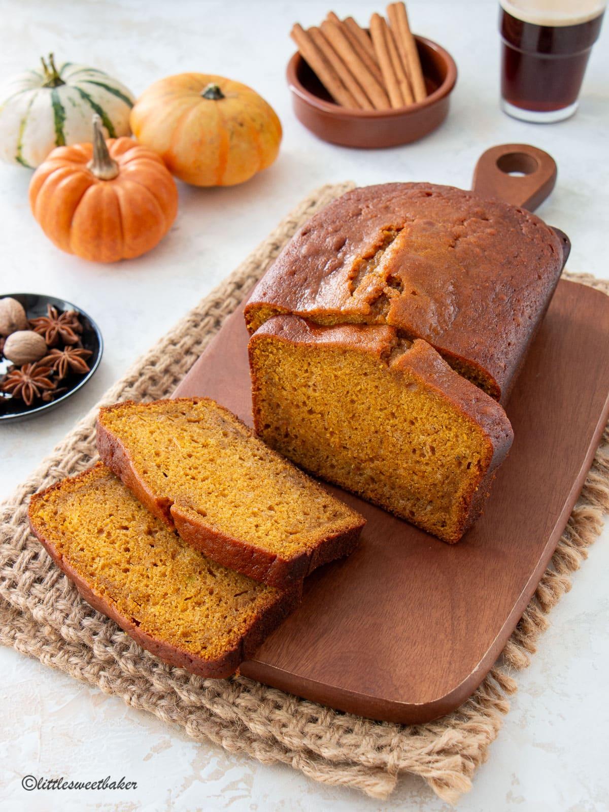 freshly baked pumpkin bread on a wooden cutting board, autumn leaves in the background