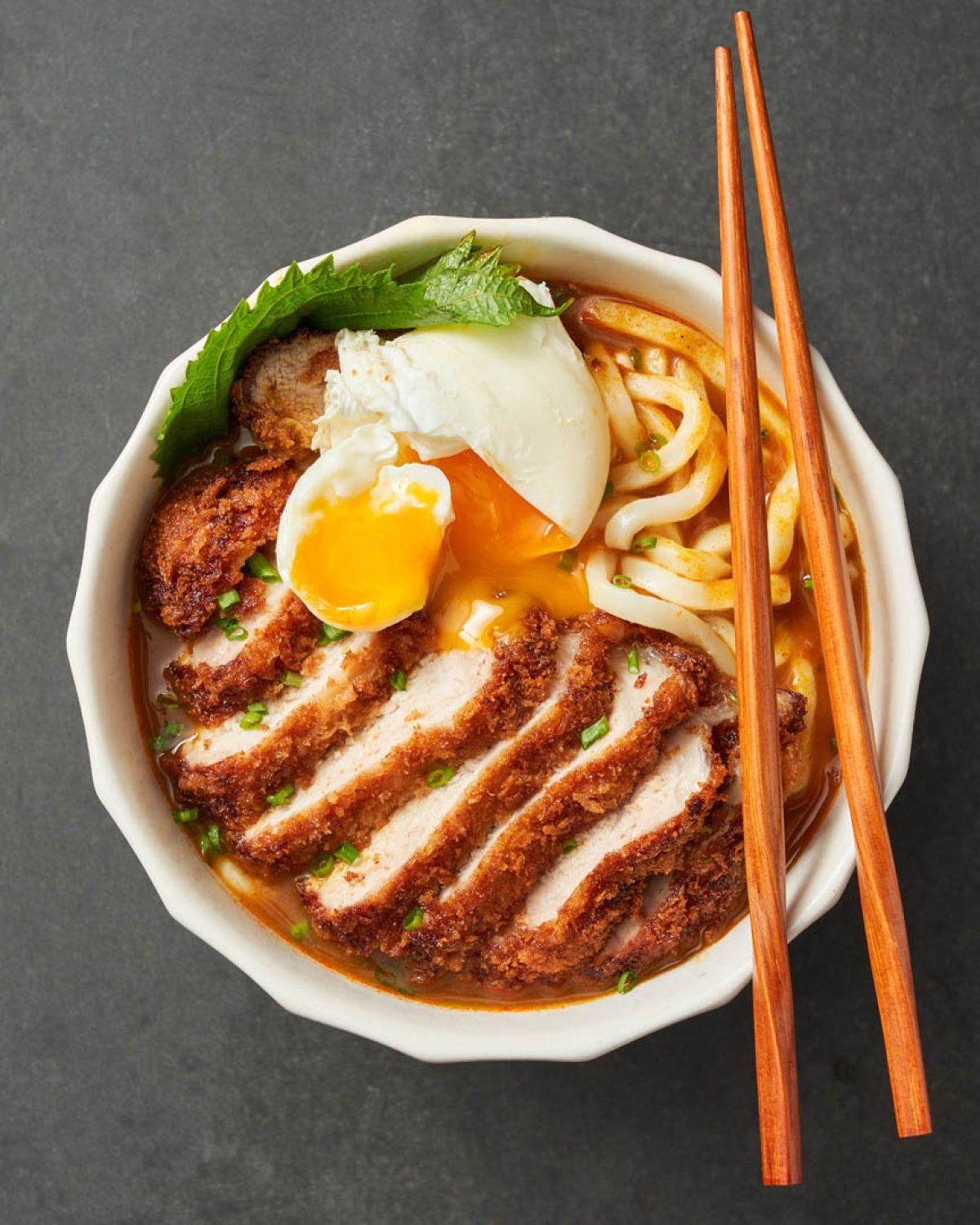 side view of a bowl of curry udon with steam rising, showing the texture of the noodles and katsu