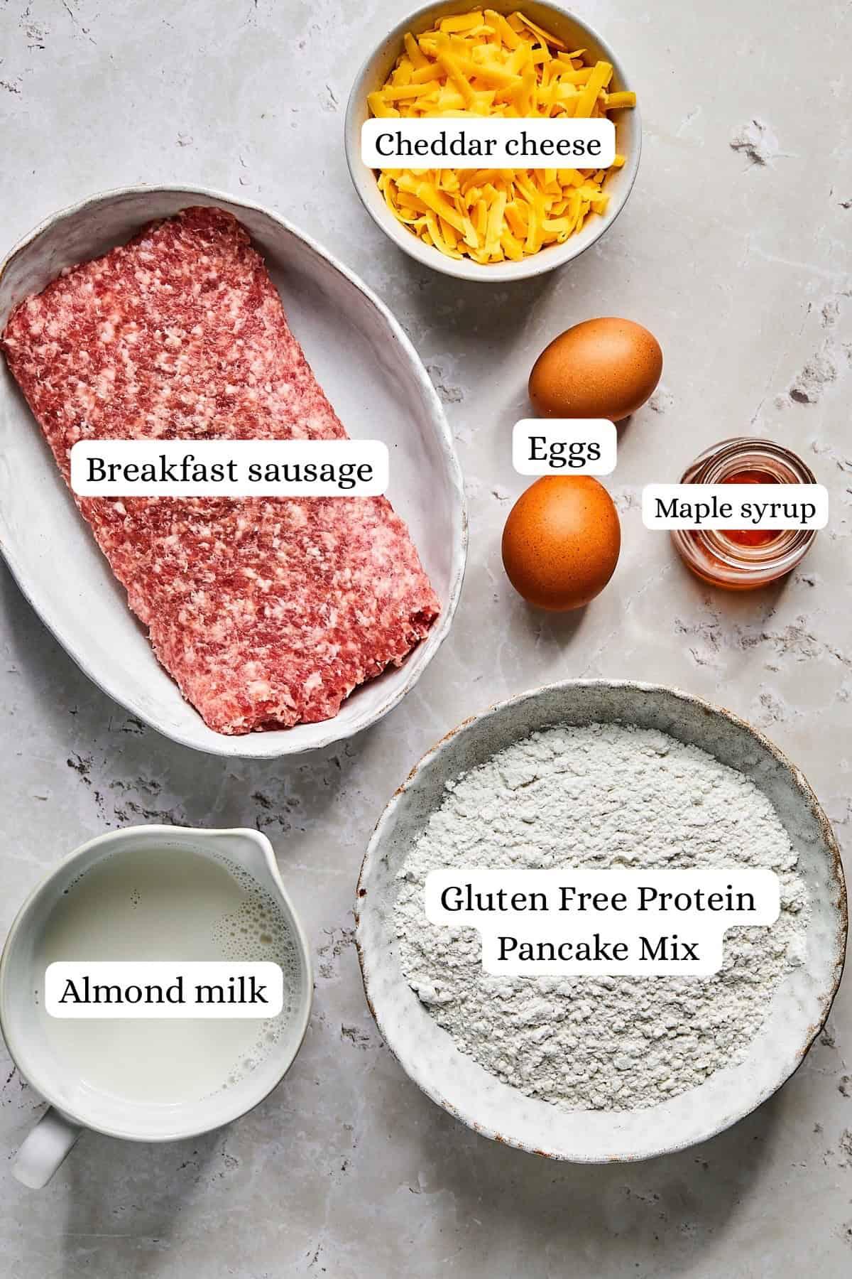 Ingredients for McGriddle bites laid out on a clean kitchen counter: pancake mix, milk, eggs, sausage, maple syrup