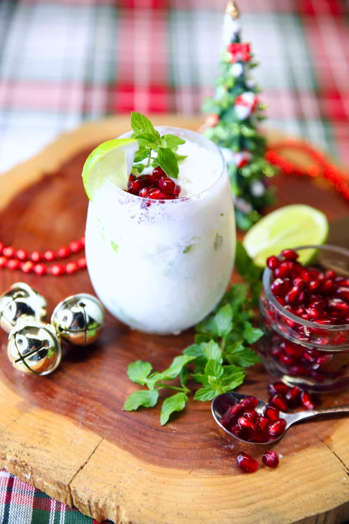 A beautifully garnished coconut mojito cocktail on a wooden tray with a backdrop of twinkling holiday lights