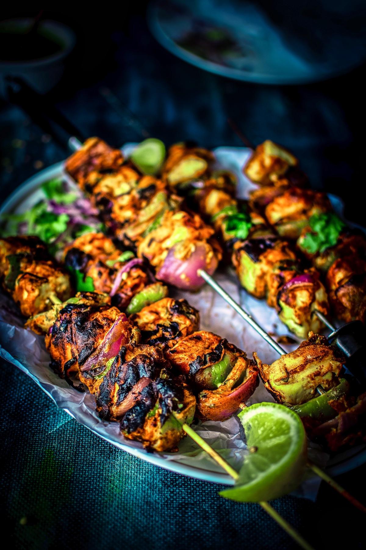 Close-up of Smoked Paneer Tikka Skewers being grilled over charcoal, smoke billowing around