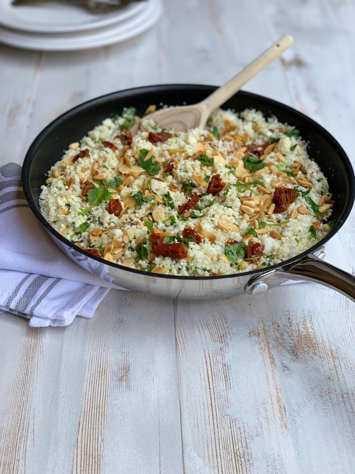 A person preparing cauliflower rice with sun-dried tomatoes in a kitchen