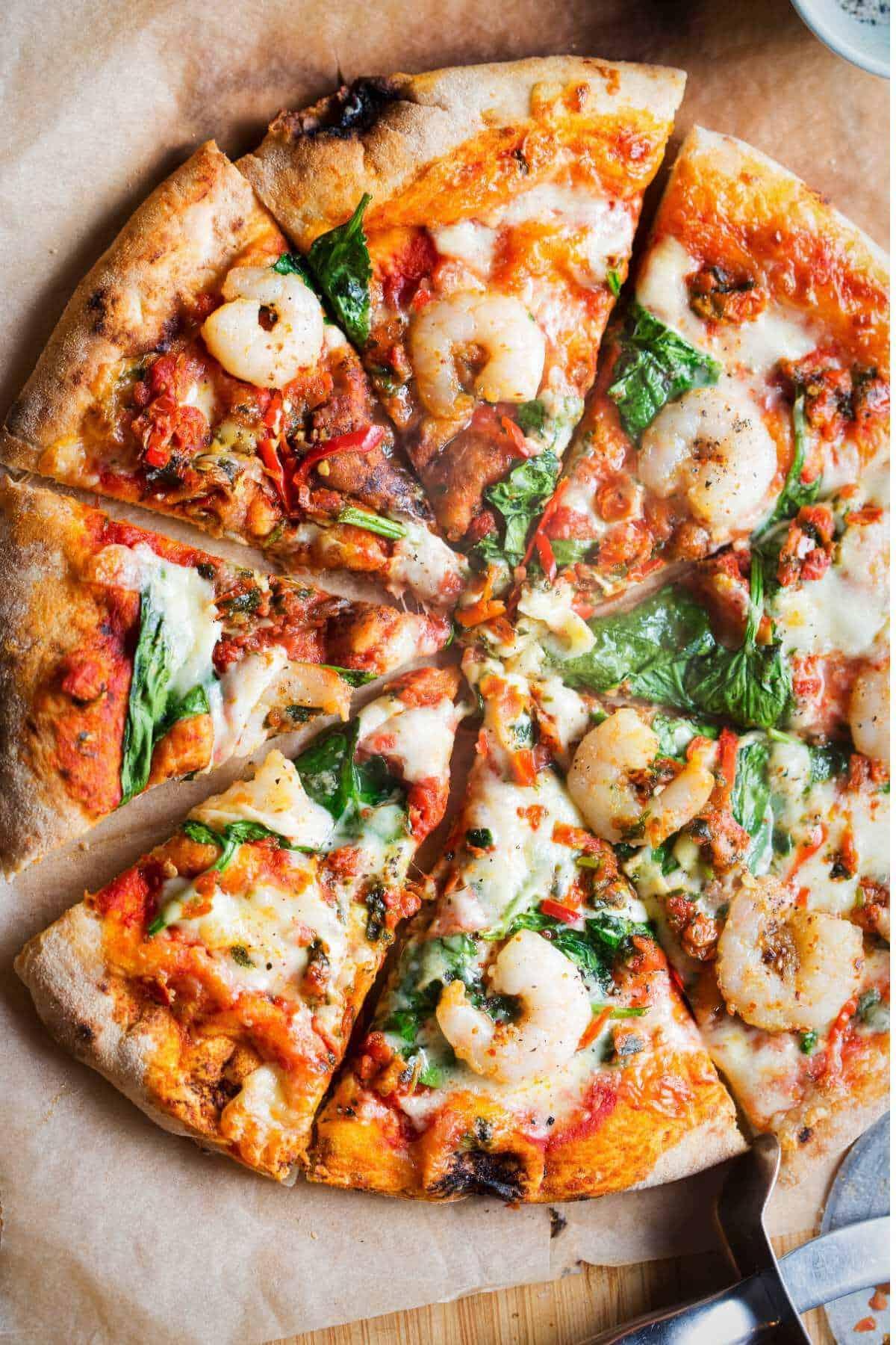Overhead shot of Malabar prawn pizza being sliced, with visible prawn and spice details