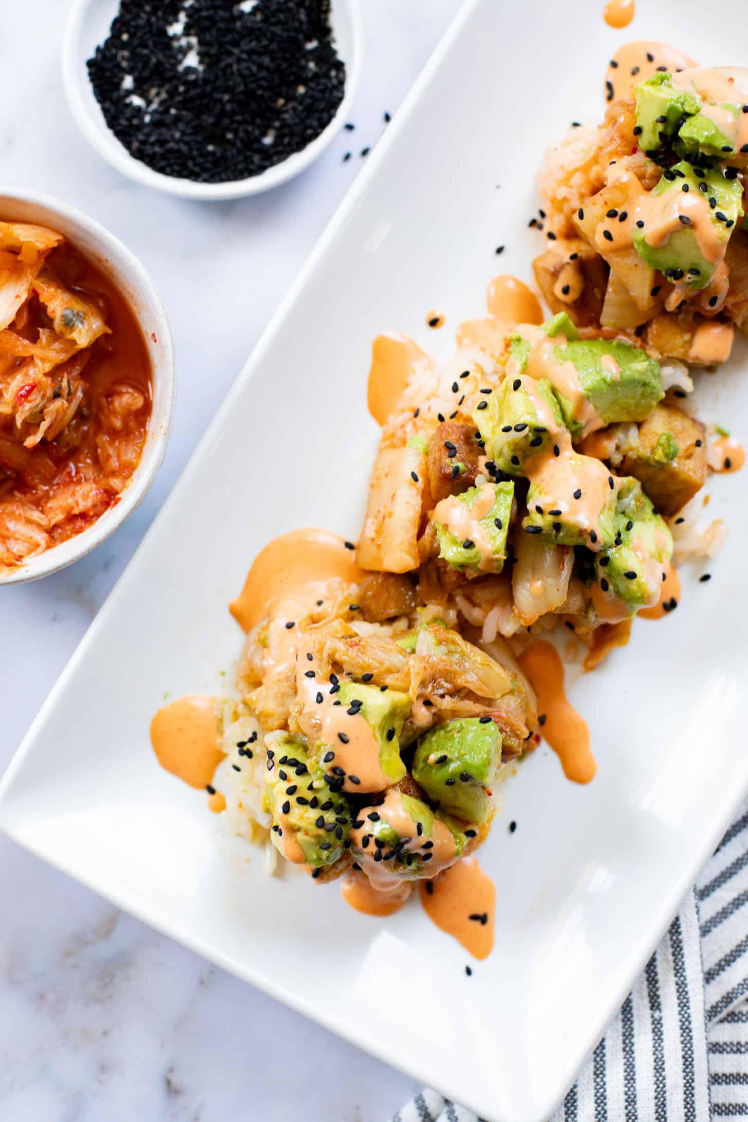 Overhead shot of several kimchi tofu burgers on a platter, garnished with sesame seeds and scallions