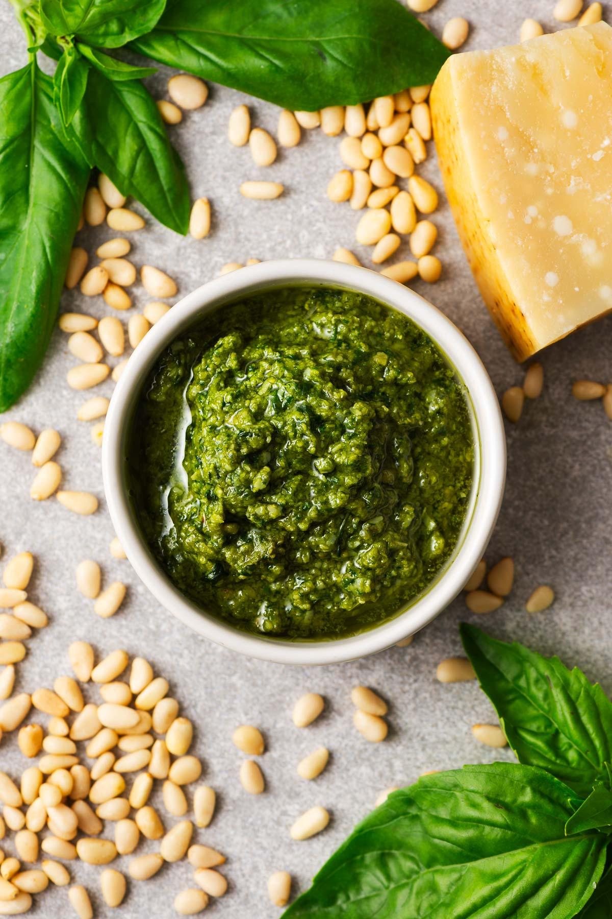 A bowl of vibrant green homemade pesto sauce, with fresh basil leaves and pine nuts visible