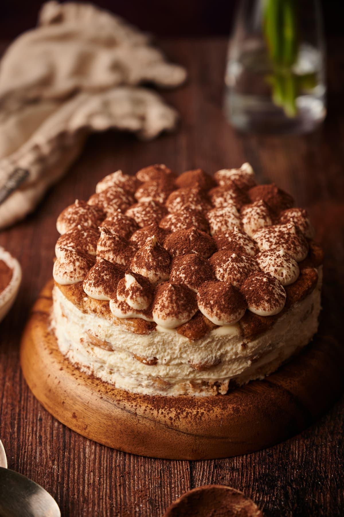 A stunning, layered tiramisu birthday cake, decorated with cocoa powder and possibly some fresh berries