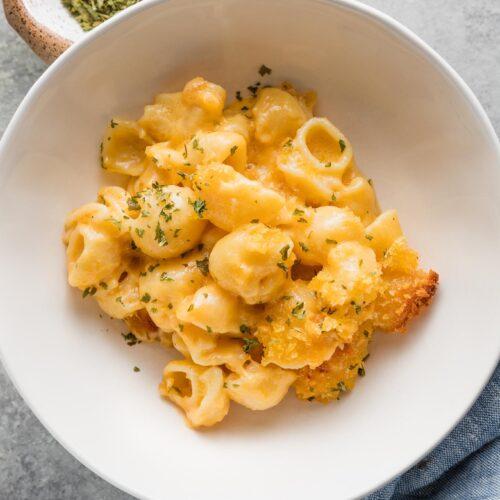 close up of a rich and creamy mac and cheese pasta bowl, garnished with fresh parsley, warm lighting