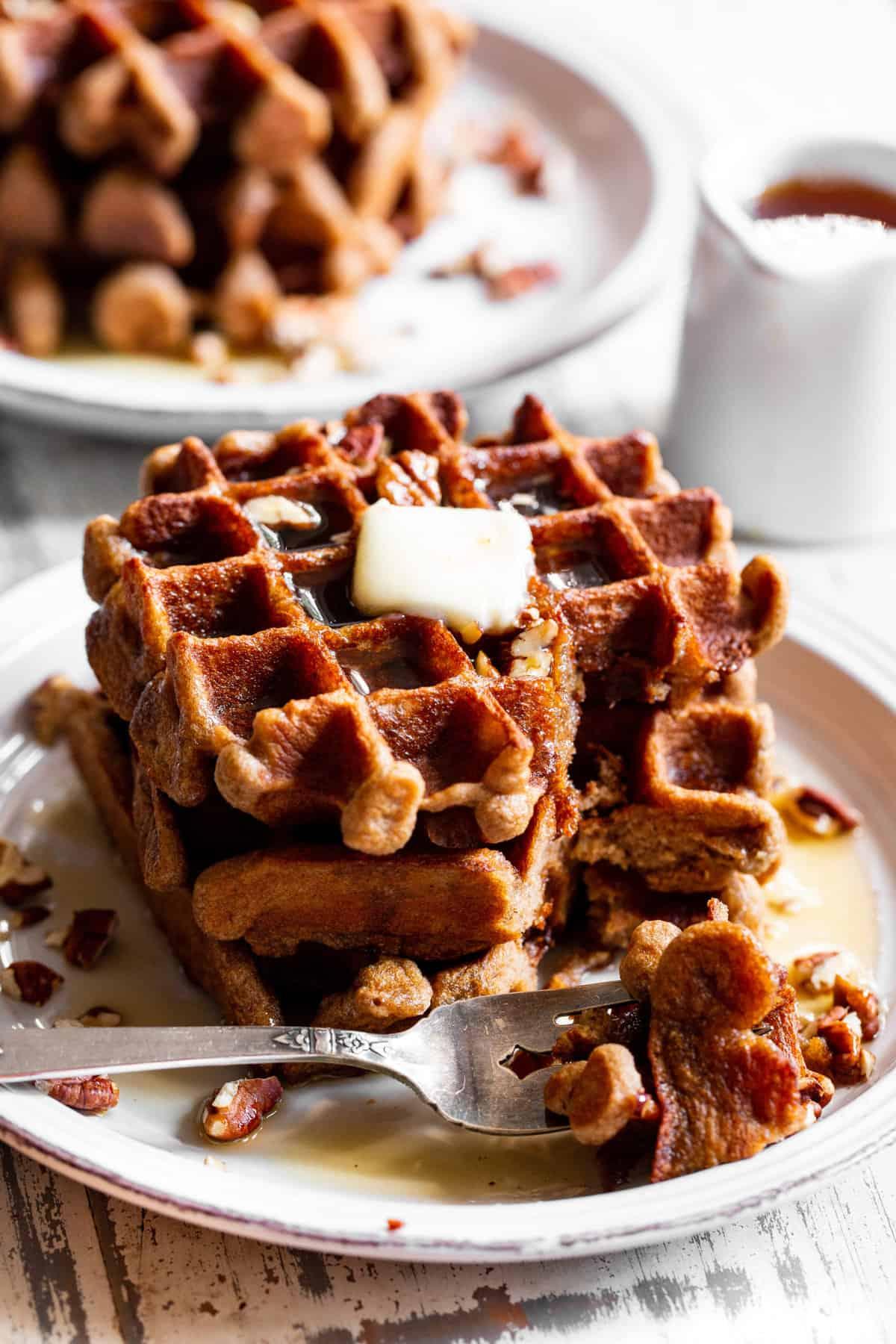 A person enjoying a plate of banana pecan waffles with maple syrup, along with a cup of coffee and a book, in a cozy setting