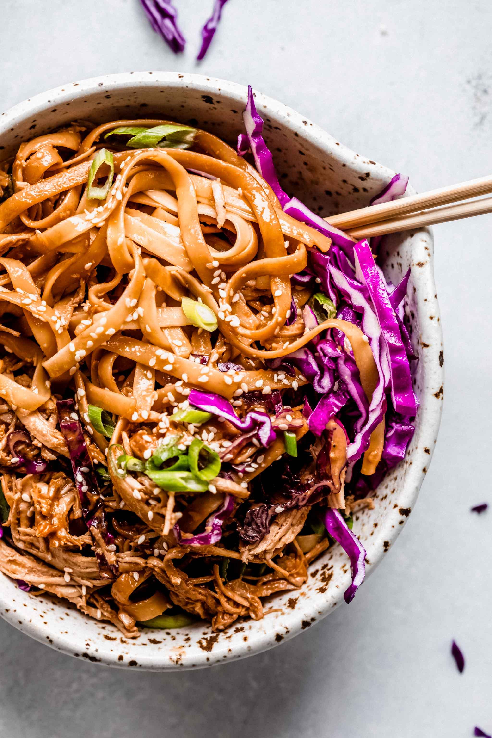 close-up shot of Thai peanut noodles being tossed with colorful vegetables and chicken