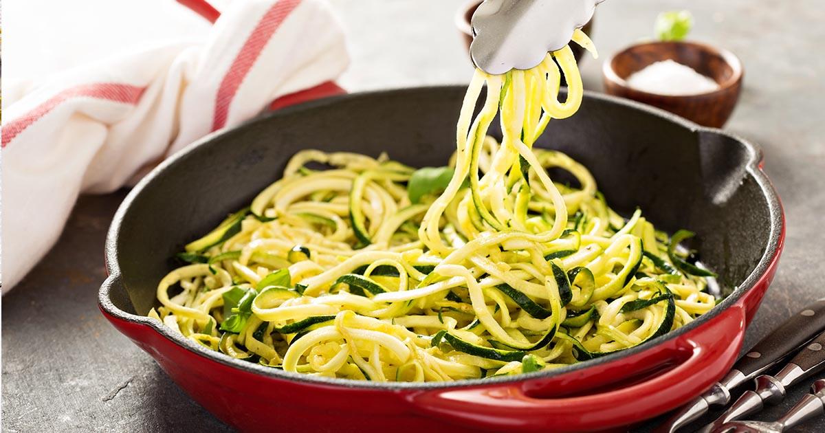 Close-up shot of garlic zoodles being tossed in a skillet, showing the steam rising and the vibrant colors of the vegetables.