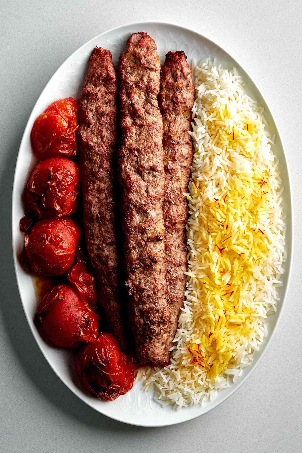 A hand placing Iranian Koobideh Beef Kebabs on a plate