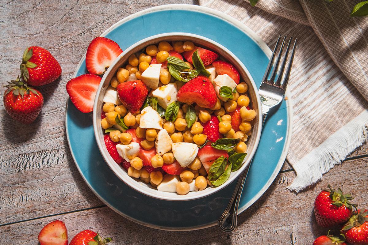 a hand tossing the strawberry and chickpea salad with the dressing
