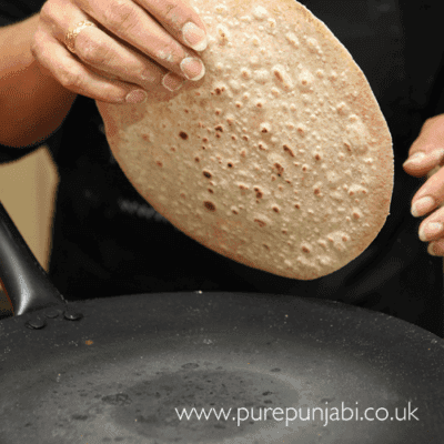 Close-up of a hand tearing off a piece of roti to dip into mango chutney