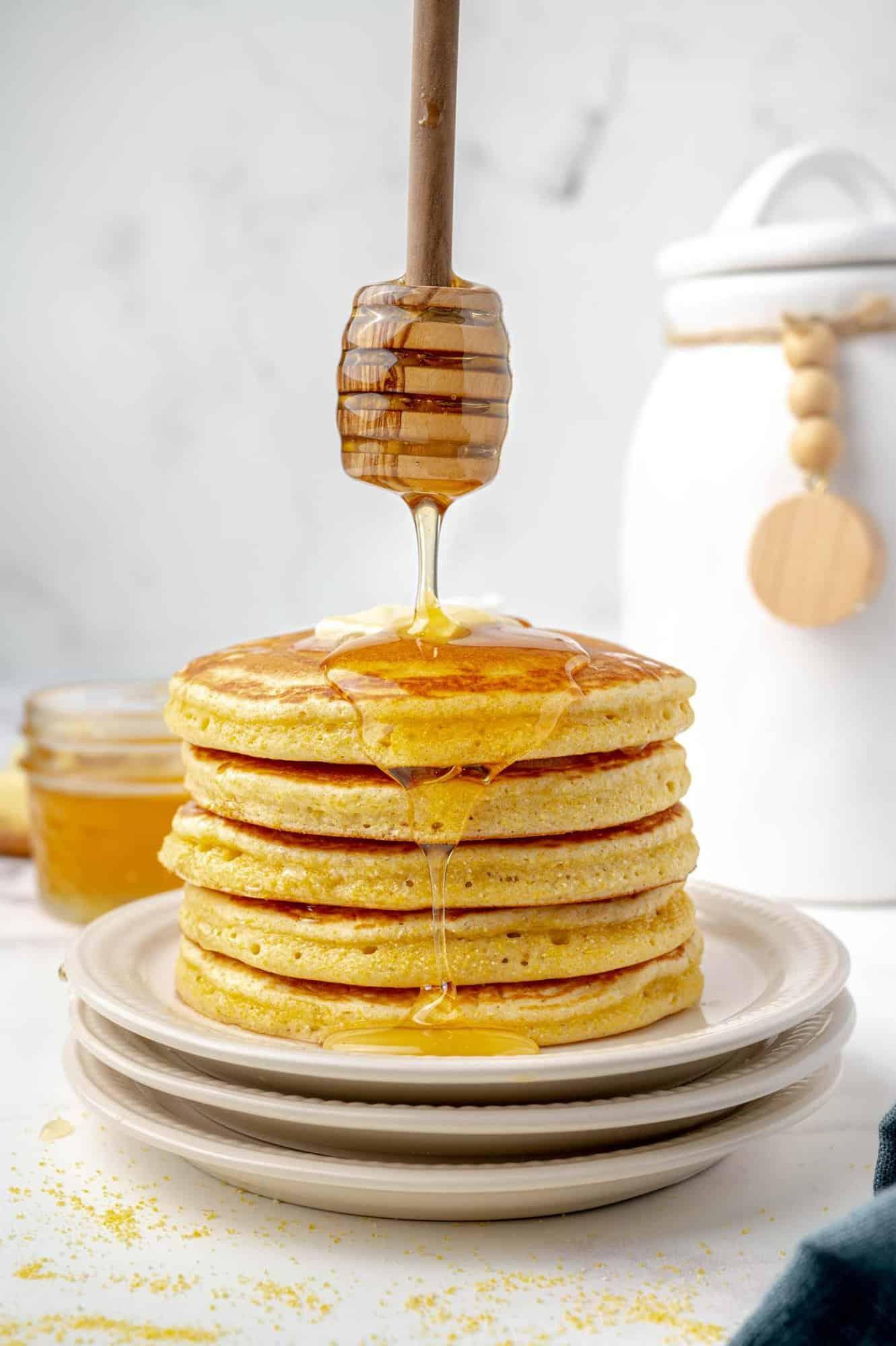 Stack of golden brown cornbread pancakes with a dollop of chili honey butter