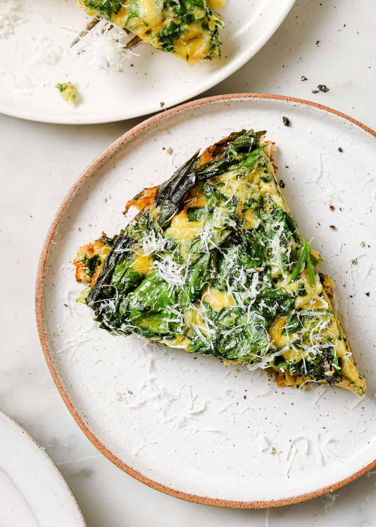 a person holding a slice of the zero-waste frittata, with a bite taken out, showcasing the texture and layers