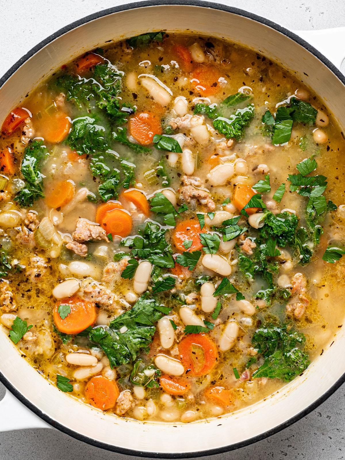Close-up shot of a bowl of kale and white bean soup with sausage, steam rising