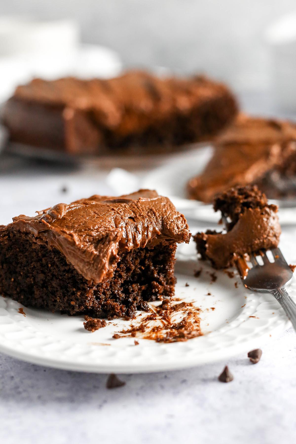 close-up shot of a slice of moist almond flour chocolate cake with a rich crumb, dusted with cocoa powder, on a vintage plate, with a fork