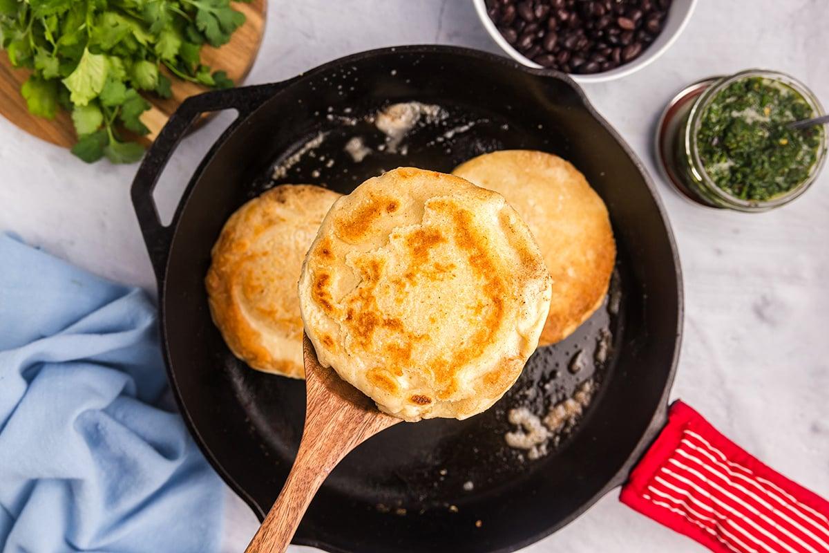 Overhead shot of golden brown arepas cooking on a griddle