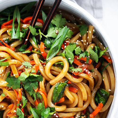 a bowl of banana udon noodle stir-fry garnished with sesame seeds and green onions