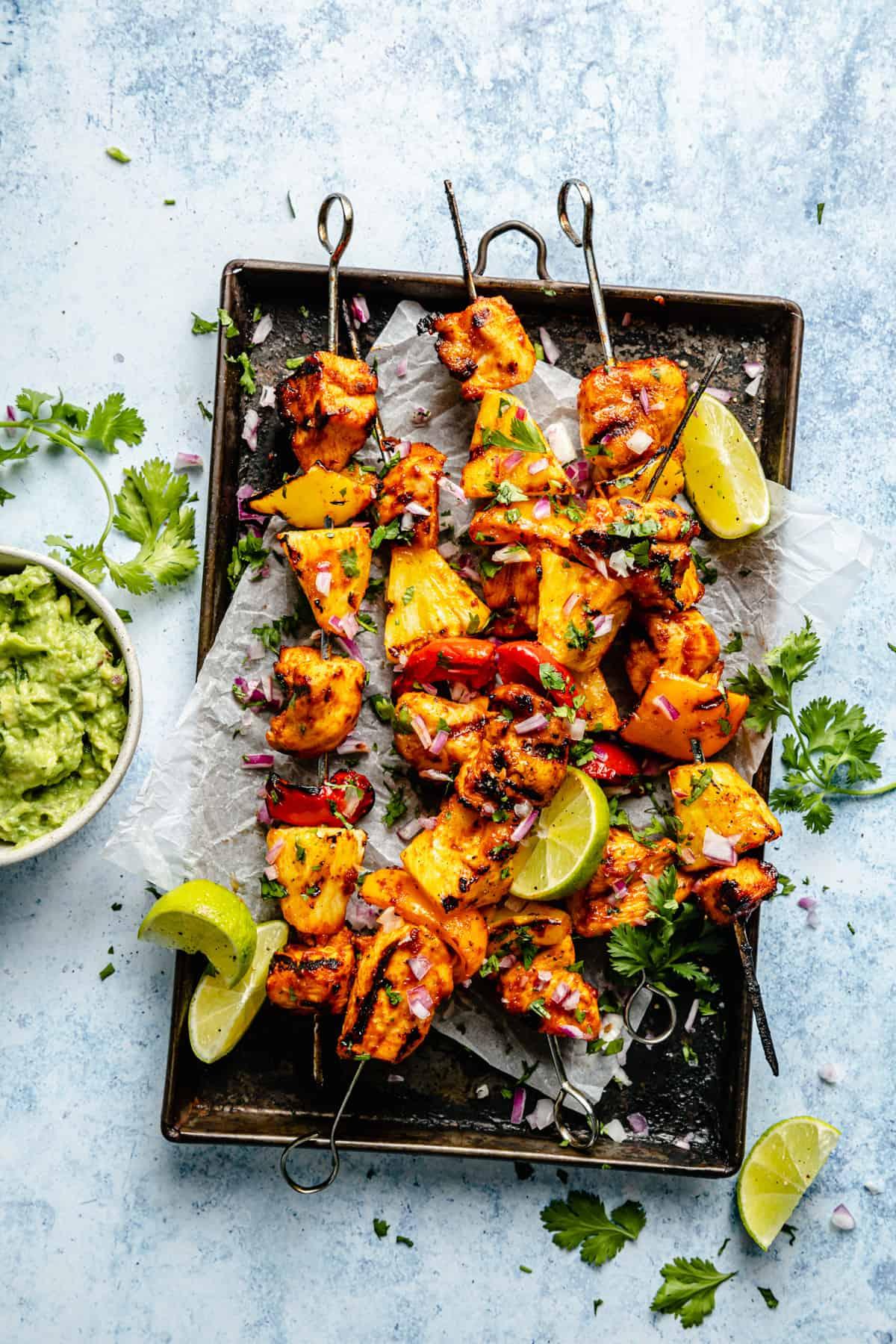a well-lit cocktail served with a small jerk chicken skewer, garnished with lime