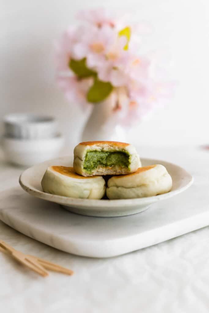 A batch of freshly steamed matcha custard buns arranged on a plate