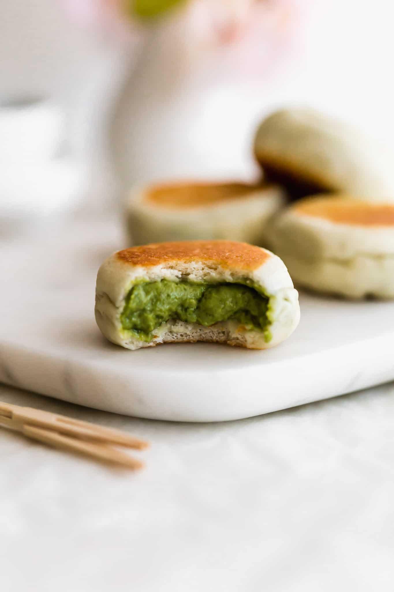 Close-up of a matcha custard bun being pulled apart, revealing the creamy custard filling