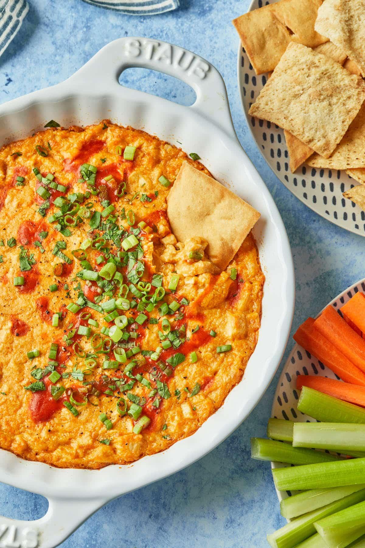 Delicious buffalo chicken dip in a baking dish, garnished with green onions and served with tortilla chips