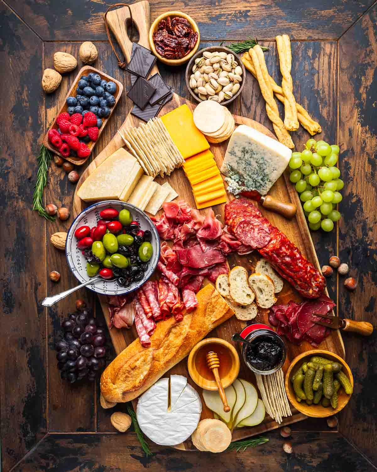 An overhead shot of a beautifully arranged cheese board with various cheeses, fruits, nuts, and accompaniments