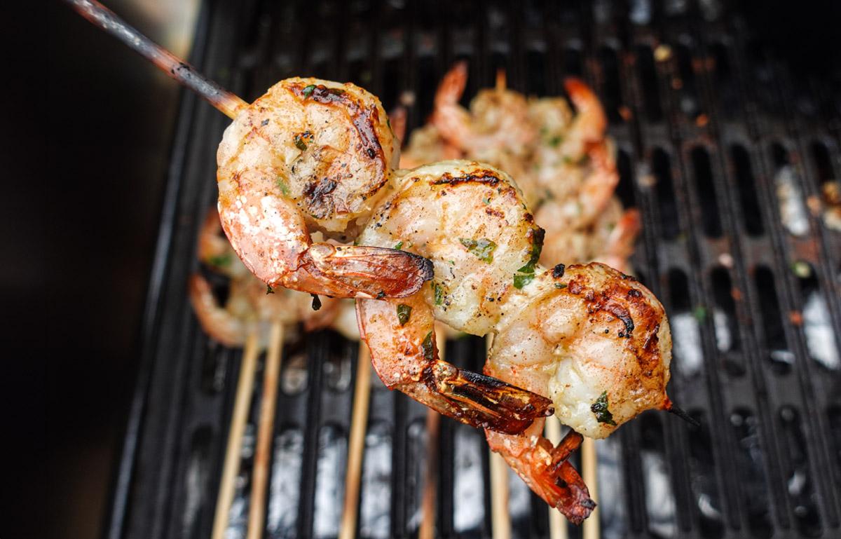 a person grilling shrimp skewers on an outdoor grill